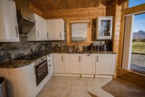 cocina con armarios blancos y ventana grande en Lorien Lodge, en Breakish