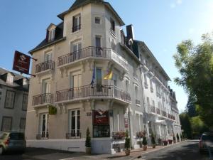 Un grand bâtiment blanc avec balcon se trouve dans une rue. dans l'établissement Hôtel de l'Aviation, à La Bourboule