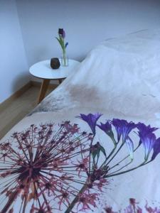 a bed with a white blanket with purple flowers on it at Annex in Oudenaarde