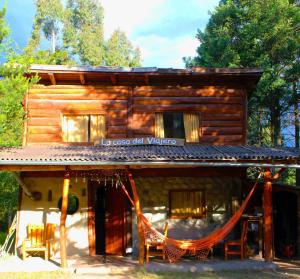 una cabaña de madera con una hamaca frente a ella en La Casa del Viajero Hostel en El Bolsón