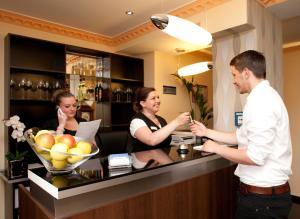 Ein Mann und zwei Frauen sitzen in einer Bar mit einem Barkeeper. in der Unterkunft Hotel City Panorama in Hannover