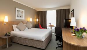 a hotel room with a bed, desk, chair and lamp at Mercure Sydney Parramatta in Sydney