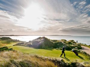 Trump International Golf Links & Hotel Doonbeg Ireland في دونبيغ: شخصان يلعبان الغولف على ملعب للجولف بالقرب من المحيط