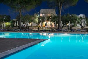 a swimming pool at night with chairs and trees at Dolmen Sport Resort in Minervino di Lecce