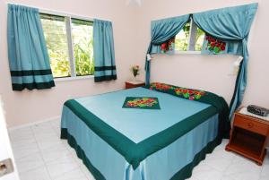 a bedroom with a bed with blue sheets and windows at Sunhaven Beach Bungalows in Rarotonga