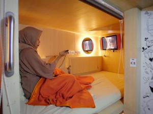 une femme assise sur un lit dans une pièce dans l'établissement INAP at Capsule Hostel, à Bandung