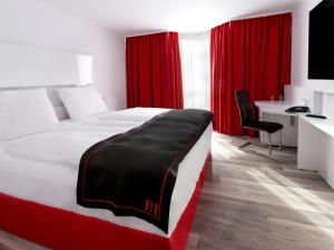 Schlafzimmer mit einem Bett mit roten Vorhängen und einem Schreibtisch in der Unterkunft DORMERO Hotel München-Kirchheim Messe in Kirchheim
