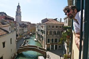 Ein Mann steht auf einem Balkon mit Blick auf einen Kanal. in der Unterkunft B&B S.Marco in Venedig