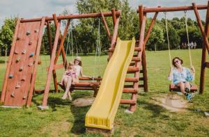 two women and a child sitting on a swing at Kempings Raganas slota in Vārve