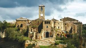 an old stone building with a clock tower on a hill at GIARDINO DI PRIMAVERA in Bagnoregio