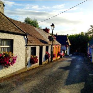 a street in a small town with flowers on buildings at Elm Cottage in Cong