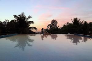 モージムにあるStayVista Ashore 6BHK Infinity Pool Ocean View- Morjimの夕日のプールの端に座る女