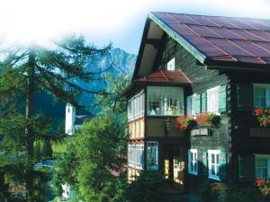 ein Haus mit einem roten Dach mit Bergen im Hintergrund in der Unterkunft Hotel Adler Garni in Hirschegg + 23 Fotos