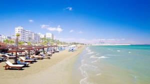 uma praia com cadeiras e guarda-sóis e o oceano em Ithaki Phinikoudes Apartments No. 106 em Lárnaca