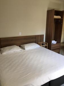 a bedroom with a large white bed with a wooden headboard at Hotel Renavi in Além Paraíba