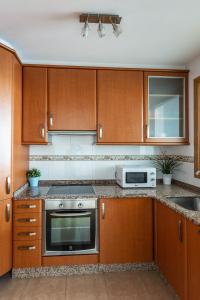 a kitchen with wooden cabinets and a stove and a microwave at APARTAMENTO EN PRIMERA LINEA DE PLAYA RiAZOR in A Coruña