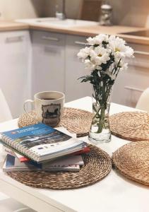 uma mesa com livros e um vaso de flores e uma chávena de café em Apartament Siódemka em Pisz