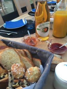 a table with a basket of bread and a bottle of orange juice at Le mas Normand in Ver-sur-Mer