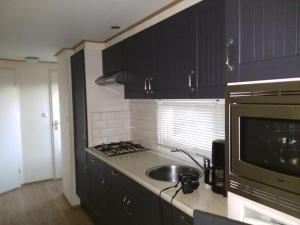 een keuken met zwarte kasten, een wastafel en een magnetron bij Chalet Seazon R23 in Buren