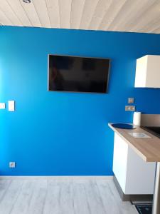 Il comprend une cuisine dotée d'un mur bleu et d'une télévision. dans l'établissement Studio Naturiste "AZUR" Héliopolis C 64, au Cap d'Agde