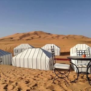 dwa krzesła i stół na pustyni w obiekcie Maroc Sahara Luxury Camp & Tours w mieście Foum Zguid