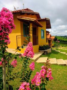 une maison jaune avec des fleurs roses devant elle dans l'établissement Pousada Divina Minas, à Três Corações