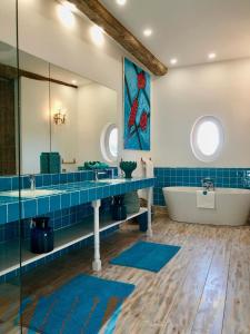 La salle de bains est pourvue de carrelage bleu, d'une baignoire et d'un miroir. dans l'établissement Bastide du régent, au Thor