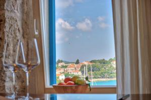 a glass of wine and a bowl of fruit in front of a window at ECO Aparthotel The Dreamers's Club in Lumbarda
