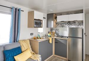 a kitchen with a stainless steel refrigerator freezer next to a couch at Le Clos des Genets in Quend