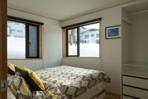 a small bedroom with a bed and two windows at Harvest House Nozawa in Nozawa Onsen