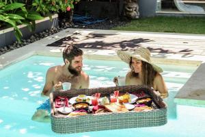 a man and woman sitting in a swimming pool with a tray of food at Kembali Villas in Seminyak