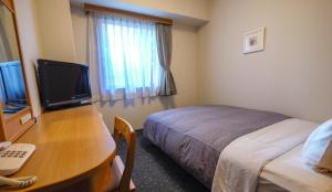 a hotel room with a bed and a desk with a television at Hotel Route-Inn Oita Ekimae in Oita