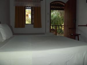 um quarto com uma cama branca e uma varanda em Pousada Flats Paguru em Búzios