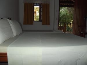 a large white bed in a bedroom with a window at Pousada Flats Paguru in Búzios