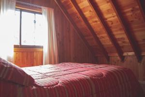 a bedroom with a bed with a wooden ceiling and a window at Cabañas Puerta del Lago in Licán Ray