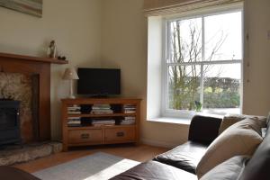 sala de estar con sofá, TV y ventana en The Hayloft Cottage en Whitby