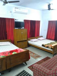 a room with three beds and red curtains at Chaiti Lodge - Santiniketan Bolpur in Bolpur