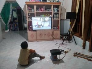 a young boy sitting on the floor watching a television at Homestay Buang Sari in Sangkapura