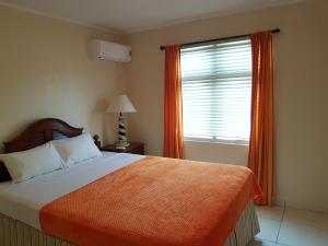 a bedroom with a bed with an orange blanket and a window at Maria Mulata Apartments in Noord