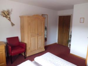 a bedroom with a red chair and a wooden cabinet at Pension Wiesengrund in Schluchsee