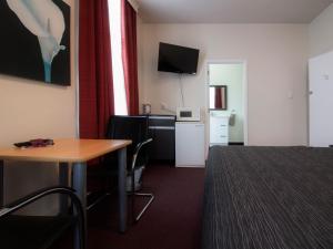 Habitación de hotel con cama, mesa y escritorio. en Masonic Hotel, en Palmerston North