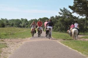 a group of people riding bikes and horses on a dirt road at Appartementen Natuurlijk in Egmond aan Zee