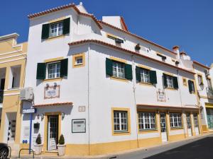 a white building with green shutters on a street at Mil Reis in Vila Nova de Milfontes