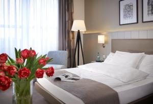 a bedroom with a bed with a vase of red flowers at Sachsenpark-Hotel in Leipzig