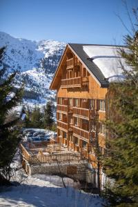 un grand bâtiment en bois avec une montagne enneigée dans l'établissement Hôtel Le Chamois d'Or, USSIM Vacances Méribel, à Méribel