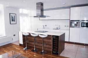 Deansgate Luxury Apartments في مانشستر: مطبخ مع دواليب بيضاء وكاونتر مع الكراسي