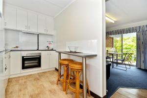 a kitchen with white cabinets and wooden stools at Dolphin Lodge Albany - Self Contained Apartments at Middleton Beach in Albany