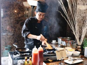 a chef cooking food in a wok on a stove at Zayn Hotel Bangkok - SHA Plus Certified in Bangkok