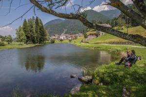 Due persone sedute sull'erba vicino a un lago di Hotel Tirol- Natural Idyll a Montesover