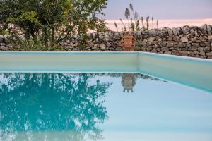 einen Pool mit einer Steinmauer und einem blauen Pool in der Unterkunft Terre di Cavalusi Relais in Donnafugata